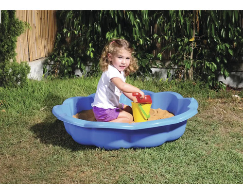 Mädchen spielt in einer blauen Sandmuschel mit Sandspielzeug im Garten.