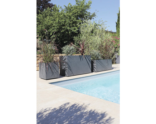 Trois jardinières grises de différentes tailles sont placées au bord de la piscine et plantées de plantes.