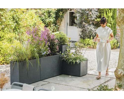 Vue de jardin avec bacs à plantes gris et une femme portant un plateau