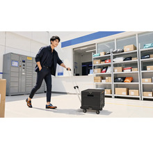 Mann zieht einen Trolley in einem Lagerraum mit Regalen und Schließfächern