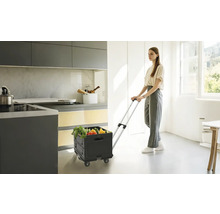 Frau zieht einen schwarzen Einkaufstrolley mit Gemüse in einer hellen Küche.