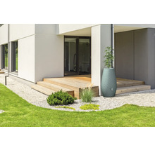 Récupérateur d'eau de pluie décoratif et jardinière à côté d'une terrasse en bois d'une maison moderne avec jardin.