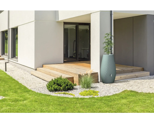 Récupérateur d'eau de pluie décoratif et jardinière à côté d'une terrasse en bois d'une maison moderne avec jardin.