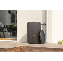 Regentonne in Holzoptik mit goldenem Wasserhahn und Deckel auf einer Holzterrasse an einer Hauswand, angeschlossen an ein Fallrohr.