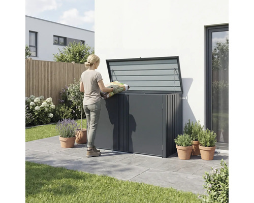 Une femme remplit un coffre de jardin avec un sac de terreau dans le jardin.