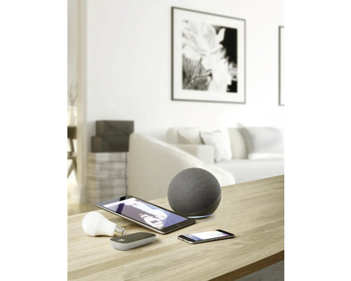 Photo d'un salon avec des appareils Smart Home tels qu'un haut-parleur, une tablette, un smartphone et une ampoule sur une table.