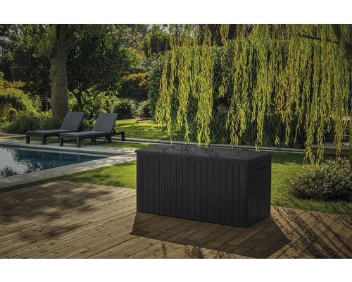 Scène de jardin avec piscine, chaises longues et grand coffre de rangement en plastique sur une terrasse en bois