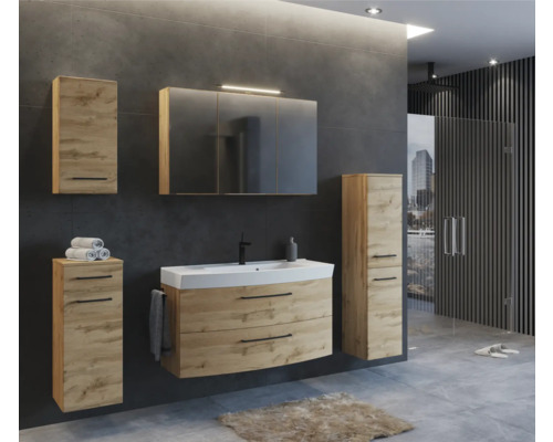 Modernes Badezimmerset in Eichenoptik mit Waschtischunterschrank, Spiegelschrank und Hochschränken vor dunkelgrauer Wand.