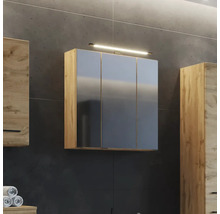 Armoire de toilette à trois portes en aspect chêne avec éclairage sur un mur sombre dans la salle de bains à côté d autres meubles en bois.