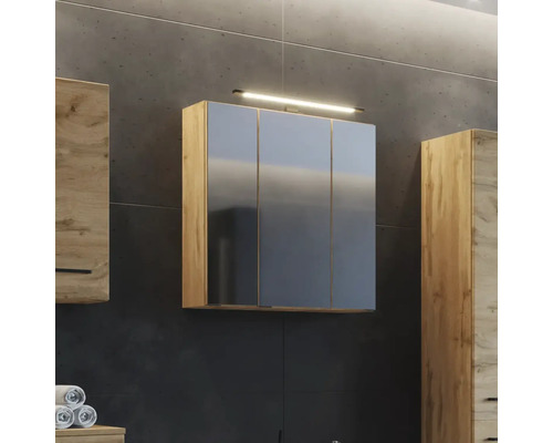 Armoire de toilette à trois portes en aspect chêne avec éclairage sur un mur sombre dans la salle de bains à côté d autres meubles en bois.