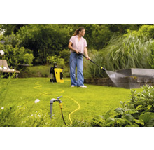 Une femme utilise un nettoyeur haute pression dans le jardin pour nettoyer un mur.