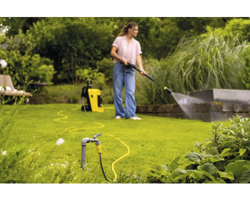 Une femme utilise un nettoyeur haute pression dans le jardin pour nettoyer un mur.