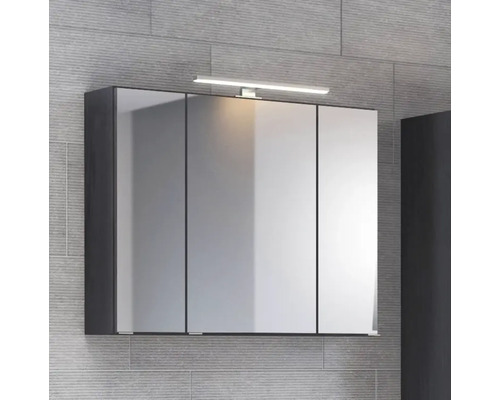 Armoire de toilette à trois portes avec éclairage LED supérieur et corps sombre sur un mur en pierre grise.