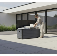 Une femme range des coussins dans un coffre de jardin gris à l'extérieur