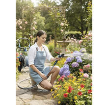 Frau bewässert Blumen mit einer Gartenspritze in einem blühenden Garten.