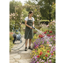 Frau bewässert Blumen mit einem Gartenschlauch neben einem Schlauchwagen in einem Blumengarten.