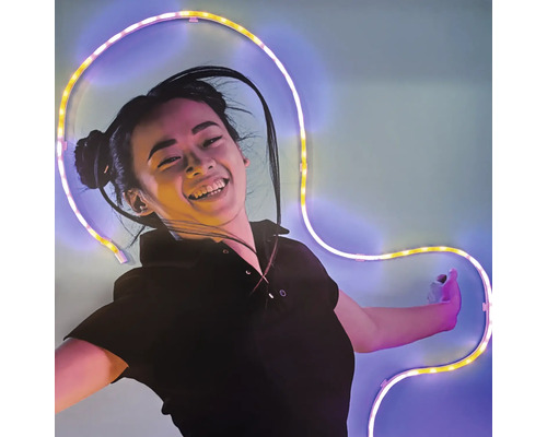 Une femme souriante devant un mur avec un ruban LED flexible et lumineux de forme incurvée.