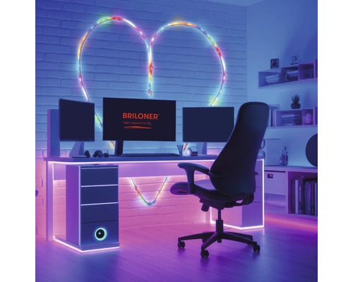 Salle de jeux moderne avec bureau, écrans et Briloner Logo. Un ruban lumineux forme un cœur sur le mur en briques derrière le bureau.