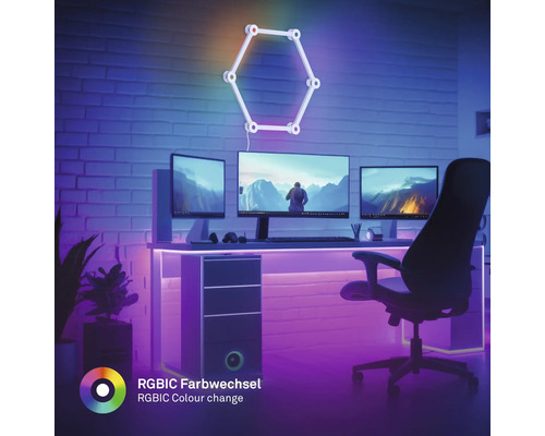 Moderner Gaming-Arbeitsplatz mit drei Monitoren, LED-Beleuchtung und hexagonaler RGBIC Wandleuchte mit Farbwechsel vor einer Ziegelwand.