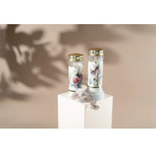 Deux bougies funéraires à motifs floraux sur un socle blanc.