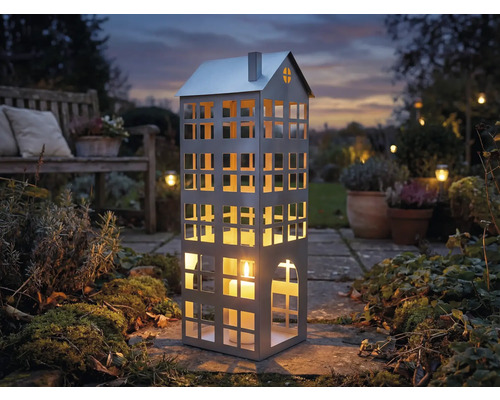 Lanterne décorative en forme de maison avec bougie dans le jardin.