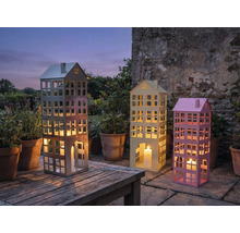 Trois photophores décoratifs en forme de bâtiments avec des bougies sur une table de jardin