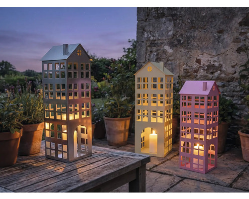Trois photophores décoratifs en forme de bâtiments avec des bougies sur une table de jardin