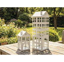 Deux lanternes décoratives blanches en métal en forme de maison sur une table en bois dans le jardin.