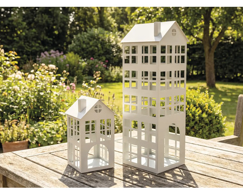 Deux lanternes décoratives blanches en métal en forme de maison sur une table en bois dans le jardin.