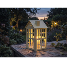 Windlicht in Hausform mit Kerze auf Holztisch im Garten