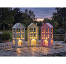 Trois lanternes décoratives en forme de maison sur une table en bois à l'extérieur.