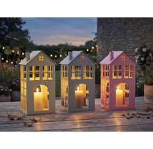 Drei dekorative Windlichter in Hausform mit Kerzen auf einem Holztisch im Garten