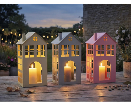 Drei dekorative Windlichter in Hausform mit Kerzen auf einem Holztisch im Garten