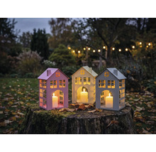 Trois lanternes en forme de maison avec des bougies sur une souche d'arbre dans le jardin