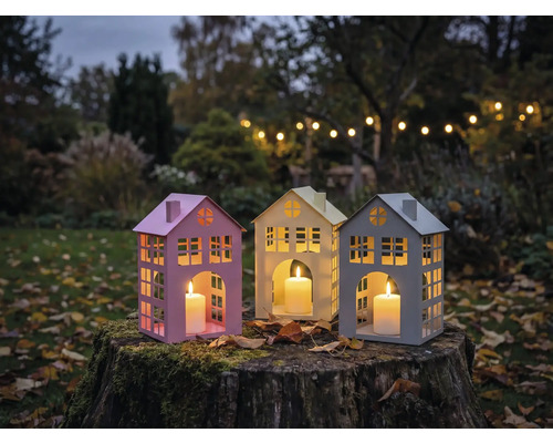 Trois lanternes en forme de maison avec des bougies sur une souche d'arbre dans le jardin