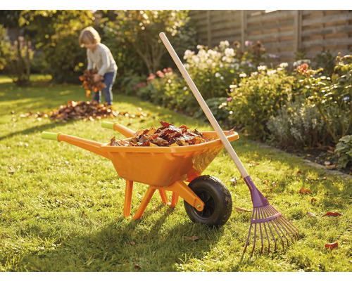 Gartenszene mit Schubkarre, Rechen und Kind beim Laubsammeln