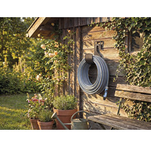 Gartenszene mit Schlauchaufroller an Holzwand, umrankt von Pflanzen