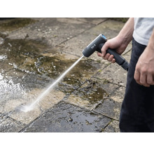 Eine Person reinigt mit einem Akku-Hochdruckreiniger Steinplatten im Aussenbereich.