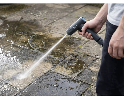 Eine Person reinigt mit einem Akku-Hochdruckreiniger Steinplatten im Aussenbereich.