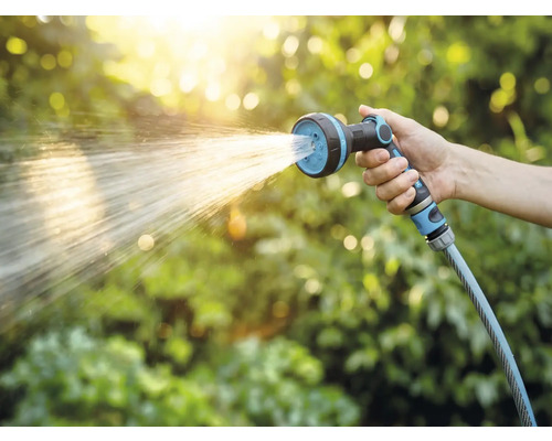 Hand hält Gartenschlauch mit Sprühkopf beim Bewässern
