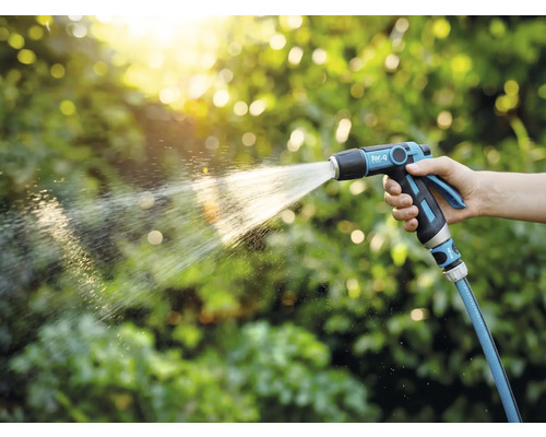 Eine Person hält eine Gartenspritze und bewässert Pflanzen.