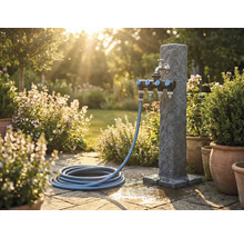 Gartenszene mit Wasserzapfsäule, Mehrfachverteiler und Gartenschlauch auf Steinterrasse