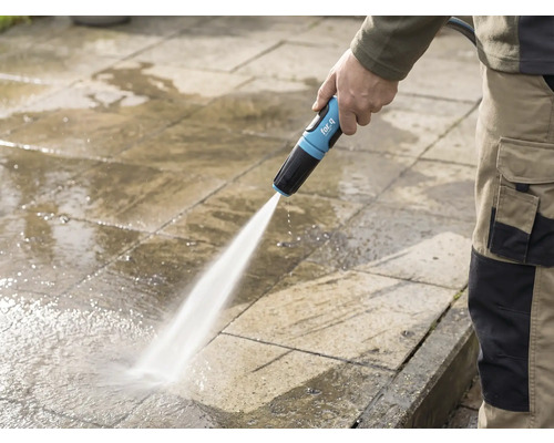 Eine Person reinigt eine Steinterrasse mit einem for_q-Gartenschlauch