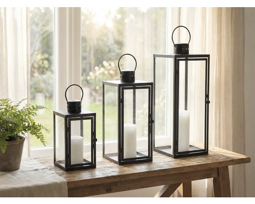 Trois photophores décoratifs en métal et verre avec bougies sur une table.