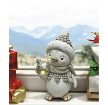 Figurine de Noël pingouin avec bonnet, écharpe et boule de Noël lumineuse sur un rebord de fenêtre devant un paysage d hiver.