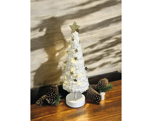 Petit sapin de Noël décoratif blanc à texture douce, cime étoilée dorée et guirlande LED étoilée sur support en bois avec pommes de pin.