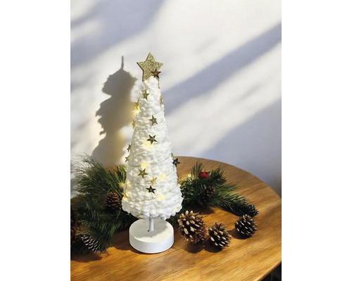 Sapin de Noël décoratif blanc avec guirlande LED et étoiles dorées sur une table en bois avec des branches de sapin et des pommes de pin.