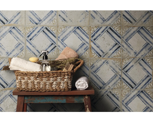 Dekorative Fliesenwand mit geometrischem Muster und Korb mit Badezimmerartikeln auf einem Hocker