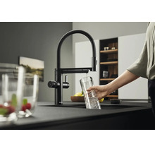 Robinet de cuisine noir avec bec pivotant et personne remplissant un verre d'eau