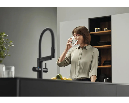 Femme buvant de l'eau dans un verre près d'un robinet dans une cuisine